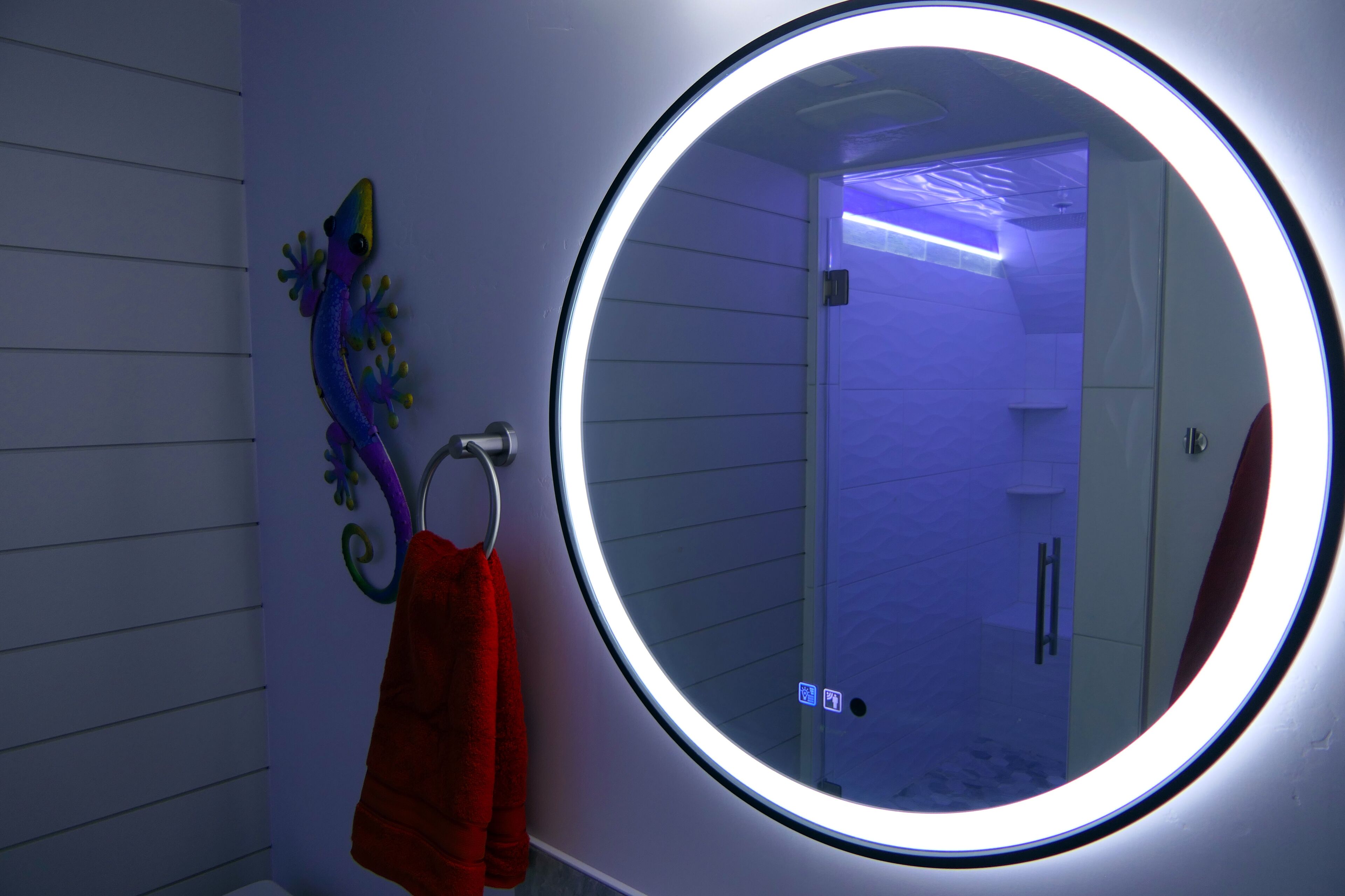A bathroom with a round mirror, a towel rack with a towel, and a decorative wall piece.