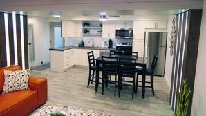 A modern kitchen with white cabinets, stainless steel appliances, and a dining area with a black table and chairs. - Natures Best Modern - Amazing GETAWAY, 2- Person LED Shower, 75" TV, King Bed (Orem)