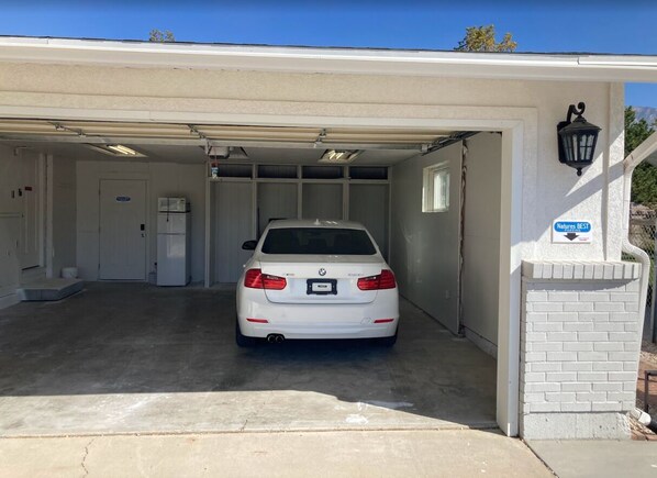 A white BMW parked in a garage with a white brick wall and a sign that reads "Natures BEST."