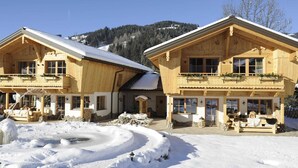 Un chalet en bois avec un toit enneigé, des fondations en pierre et un balcon en bois orné de plantes.