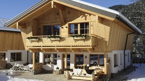 Un chalet en bois doté d’un balcon, de murs en pierre et d’un espace avec un banc en pierre.