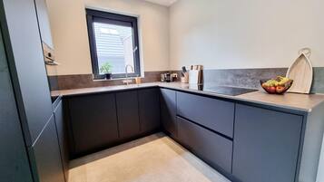 A modern kitchen with dark cabinetry, a window, and a countertop with a fruit bowl.