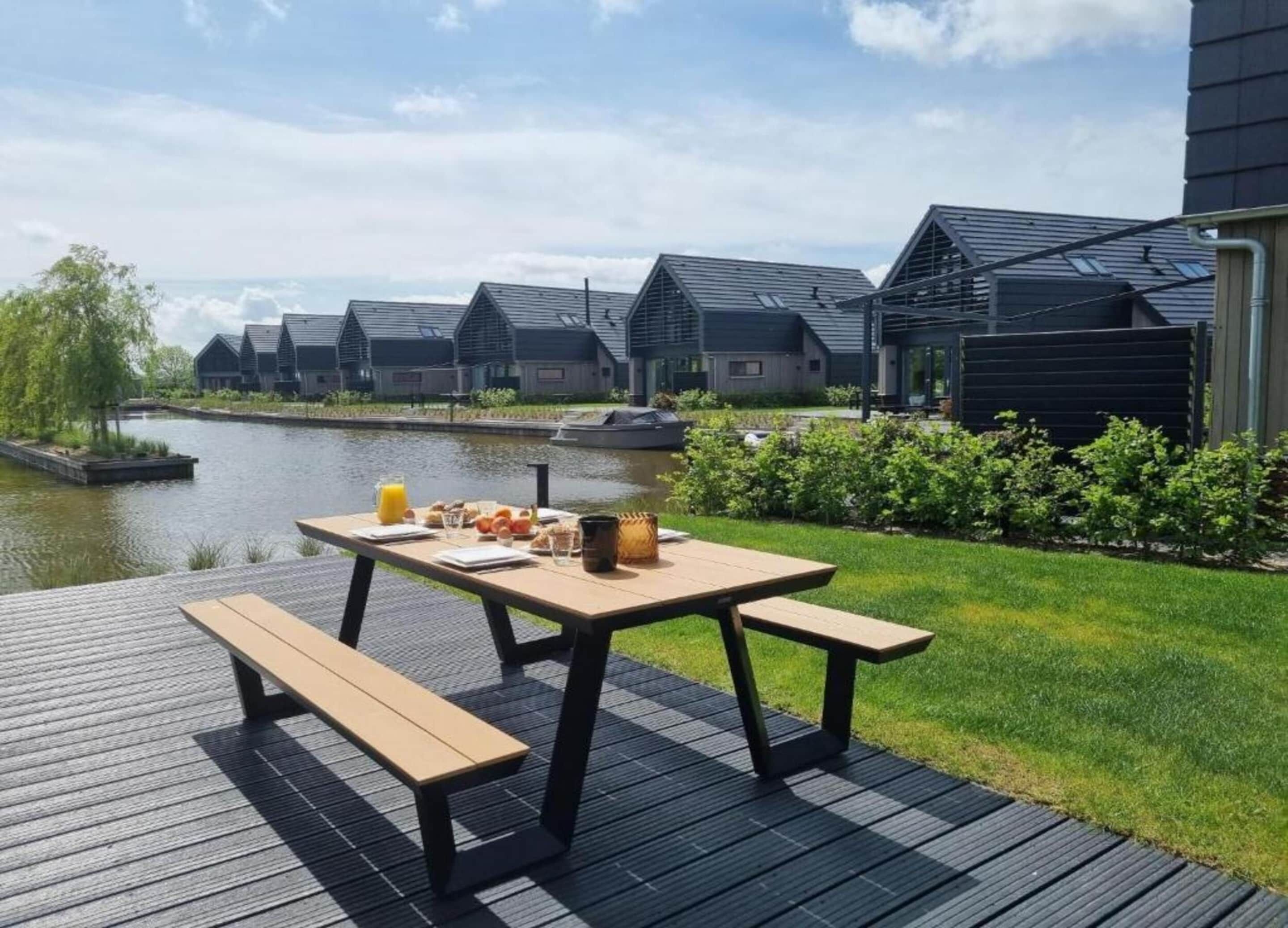 A riverside deck with a picnic table, benches, and a breakfast spread.
