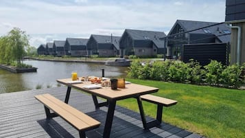 A riverside deck with a picnic table, benches, and a breakfast spread.
