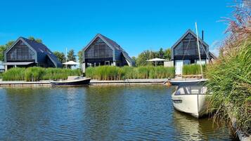 A canal with two modern buildings, a boat docked, and lush greenery.