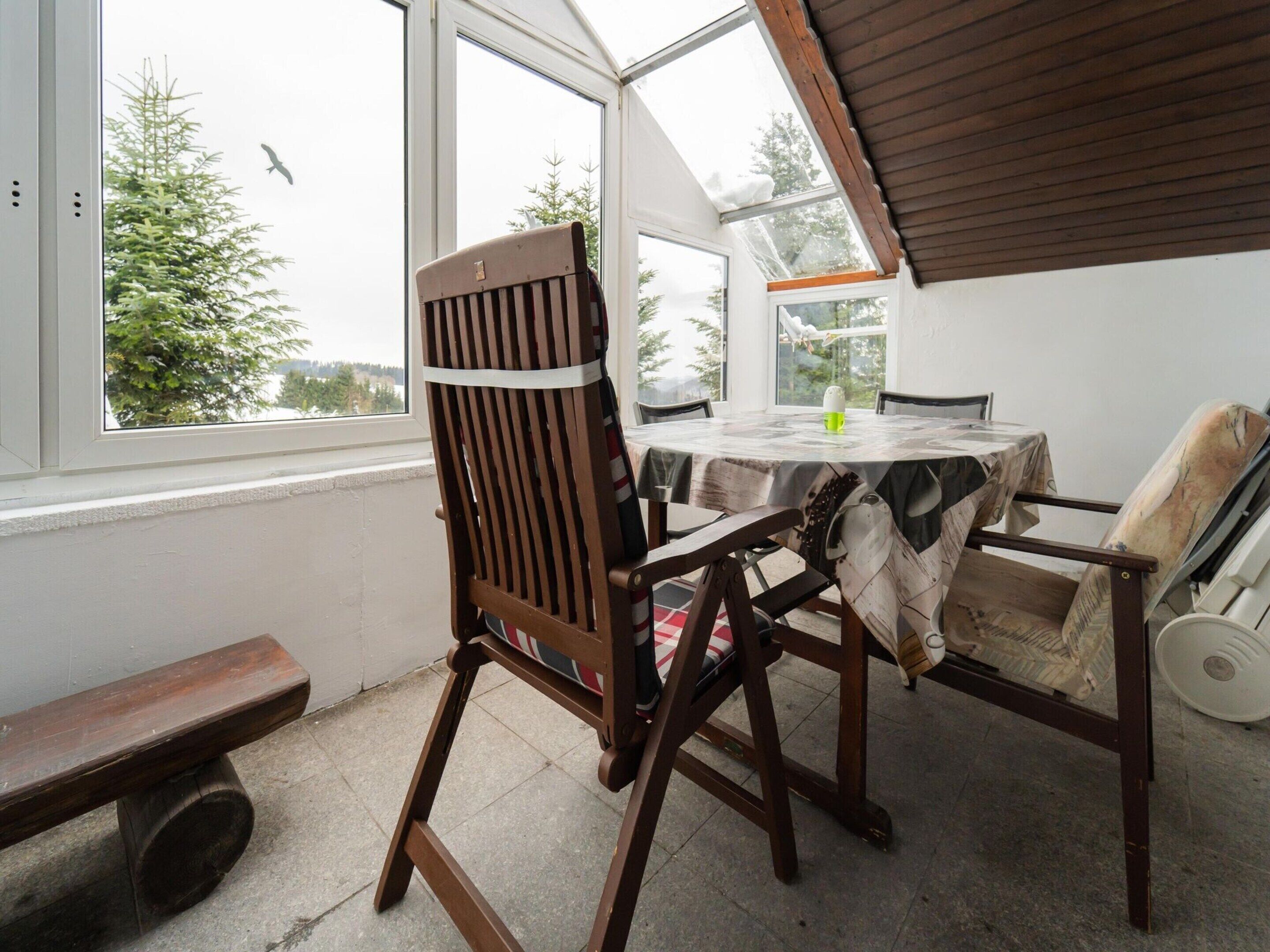 A dining area with a table and chairs, a bench, and a view through large windows.