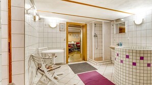 A bathroom with white tiles, a shower, a sink, and a small table with chairs. - Cozy Holiday Home With Terrace and Garden (Grossbreitenbach)