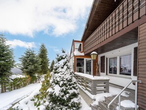 A wooden cabin with a balcony, snow-covered trees, and a clear sky.
