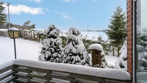 A snow-covered bench outside a building with a view of snow-laden trees and a lake. - Cozy Holiday Home With Terrace and Garden (Grossbreitenbach)