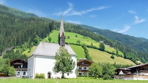 A white church with a tall steeple, surrounded by green hills and a clear blue sky. - Apartment Bramberg Near Wildkogel Ski Lift (Bramberg am Wildkogel)