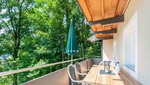 A balcony with a wooden table and chairs, a green umbrella, and a view of lush trees. - Apartment Bramberg Near Wildkogel Ski Lift (Bramberg am Wildkogel)