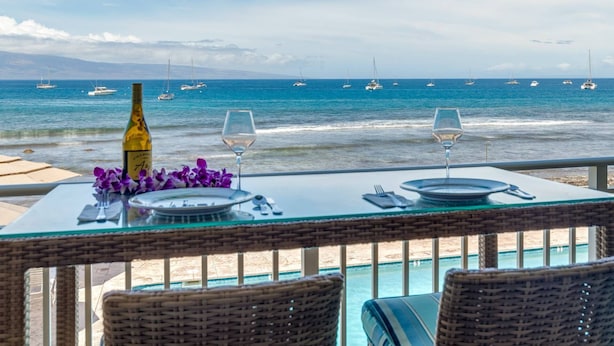 A table with a bottle and glasses, overlooking a beach with boats. - Lahaina Roads 206 - Complete remodel - Oceanfront - You can't beat the view and location! (Lahaina)