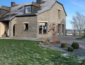 A stone house with a sloped roof, a large window, and a metal sculpture in the yard.