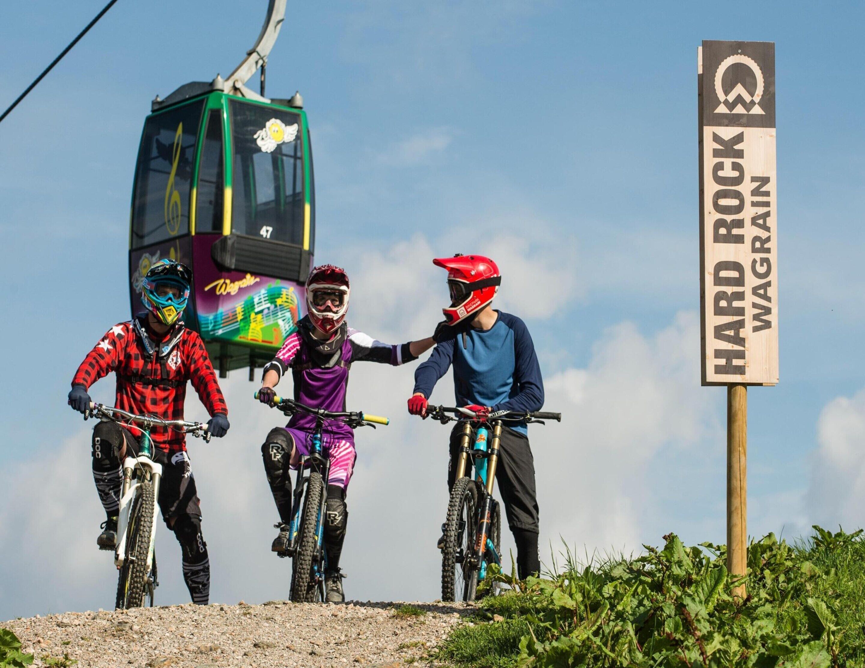 Three mountain bikers on a trail with a sign reading "HARD ROCK WAGRAIN".