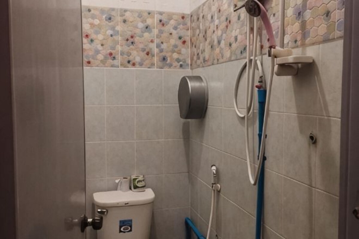 A bathroom with a toilet, a hand dryer, and a shower hose.