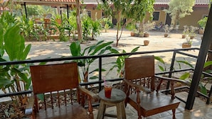 A patio with two wooden chairs and a small round table, surrounded by potted plants and a tiled floor. - erawan guesthouse (Pakse)