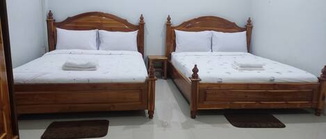 Dos camas de madera con sábanas y almohadas blancas, una mesita de noche pequeña y un cuadro colgado en la pared.