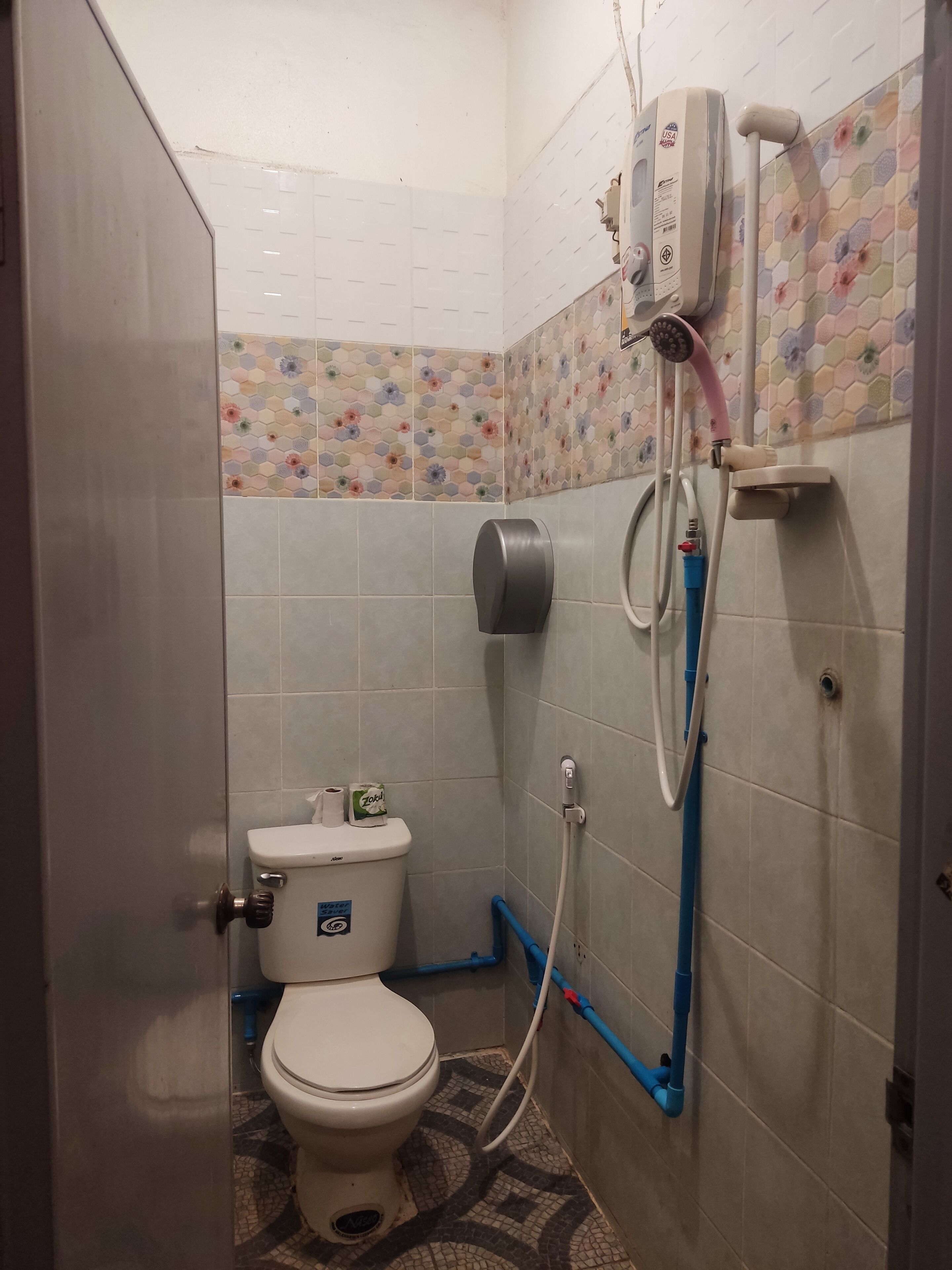 Un baño pequeño con azulejos, un inodoro, un secamanos y un cabezal de ducha.