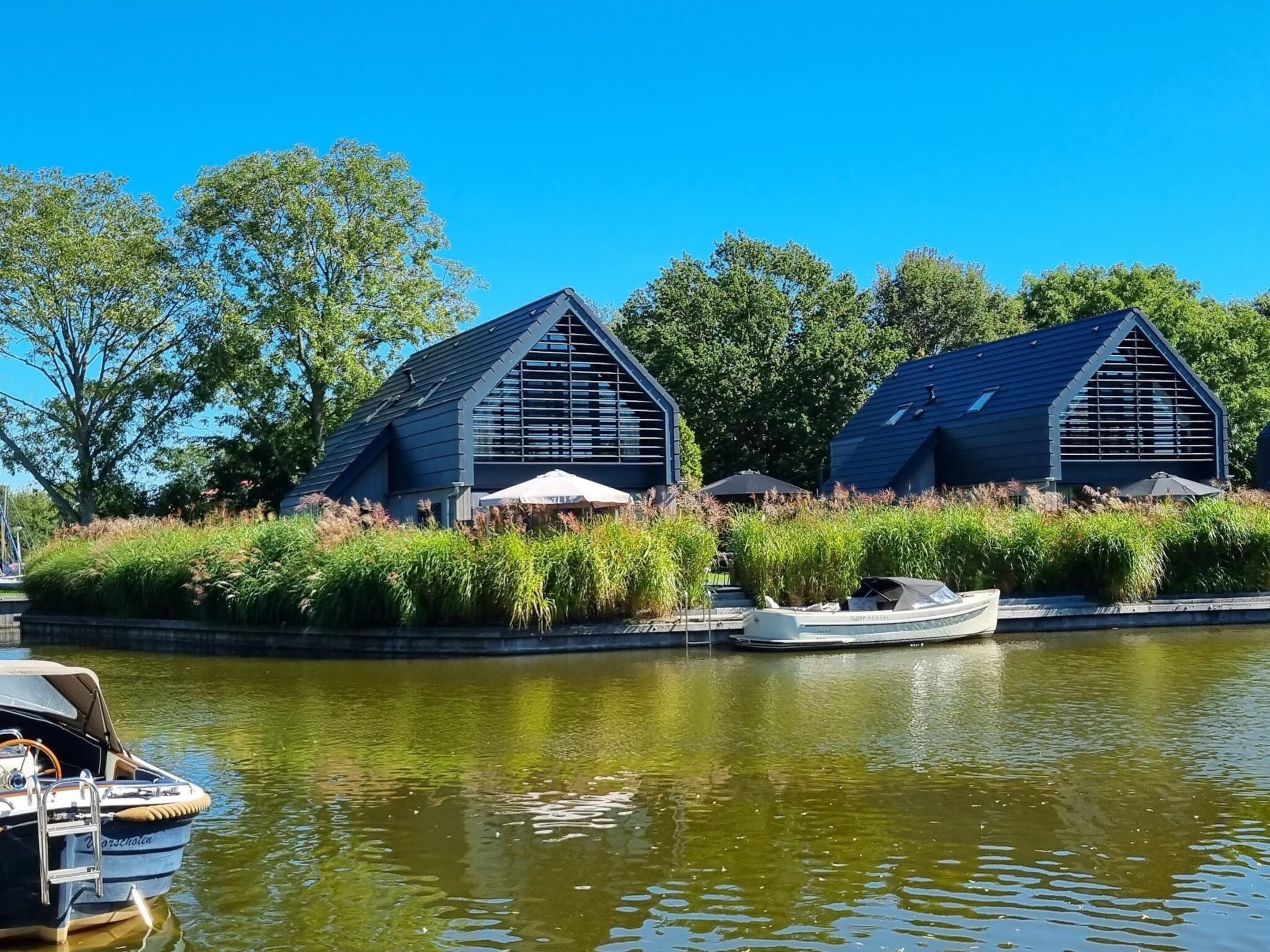 A modern building with a sloped roof, surrounded by lush greenery and a calm water body.