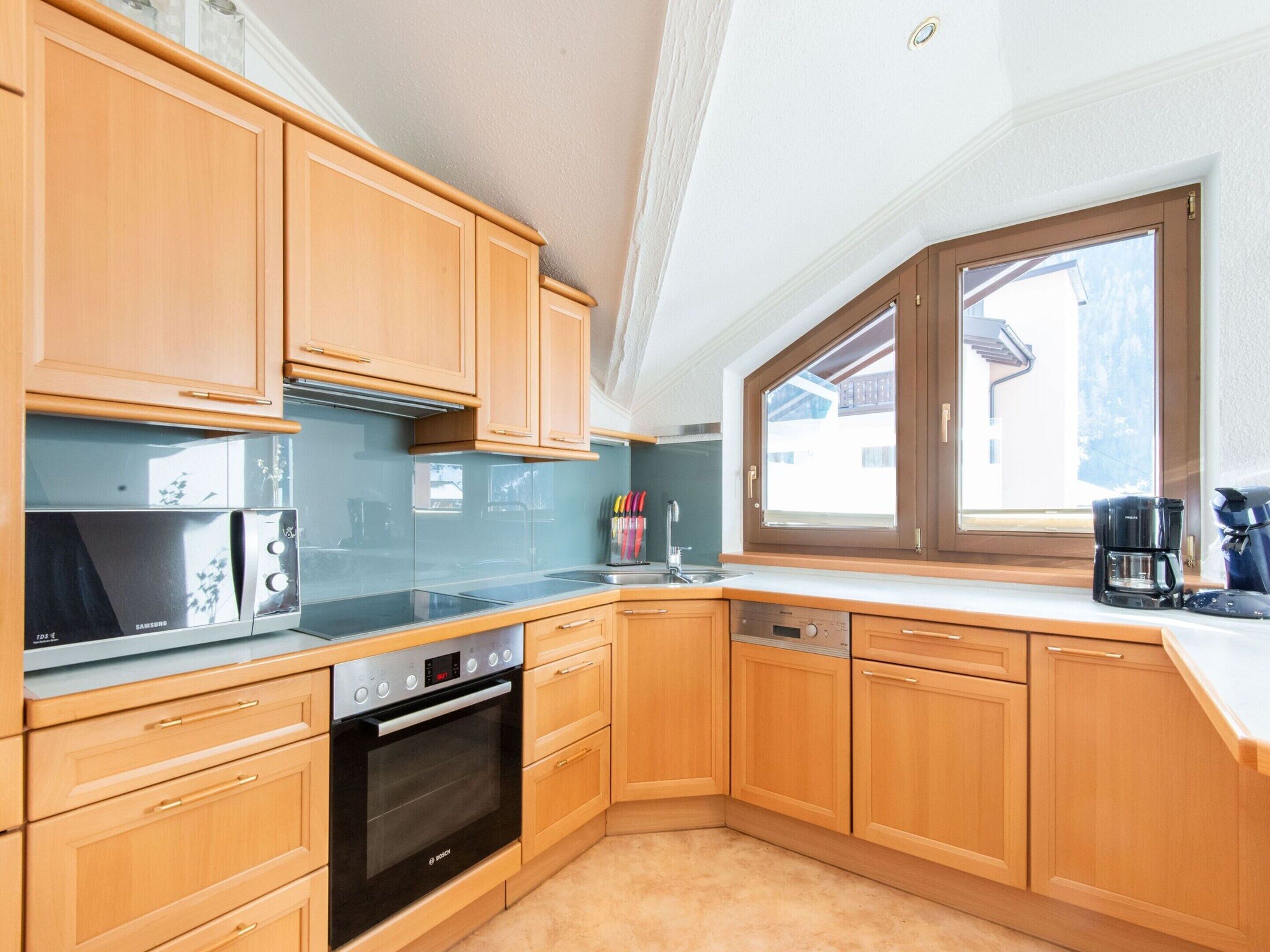 A modern kitchen with wooden cabinets, stainless steel appliances, and a large window providing natural light.