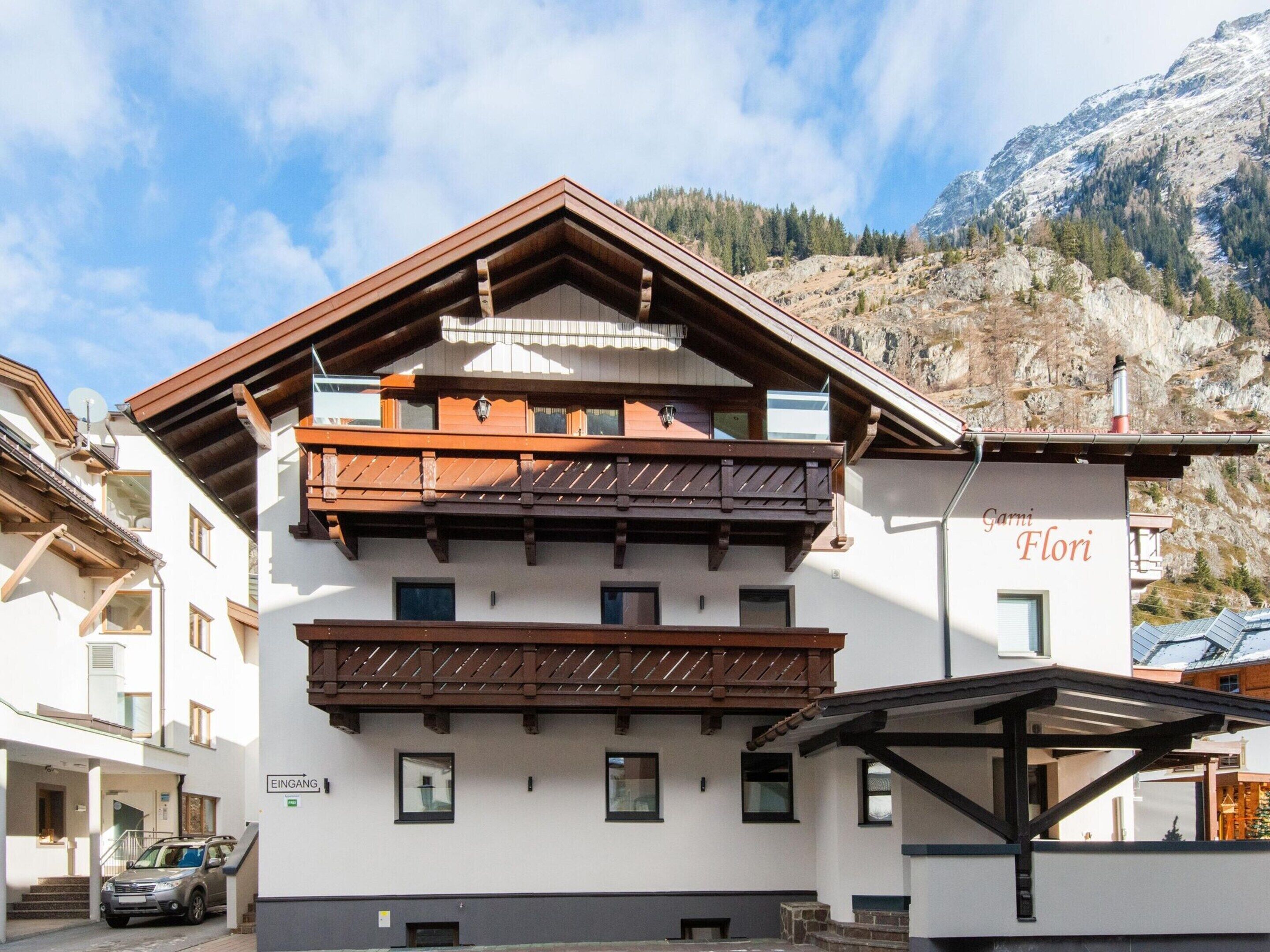 A multi-story building with a traditional Alpine architectural style, featuring wooden balconies and a sign indicating a restaurant named "Garmi Flori".