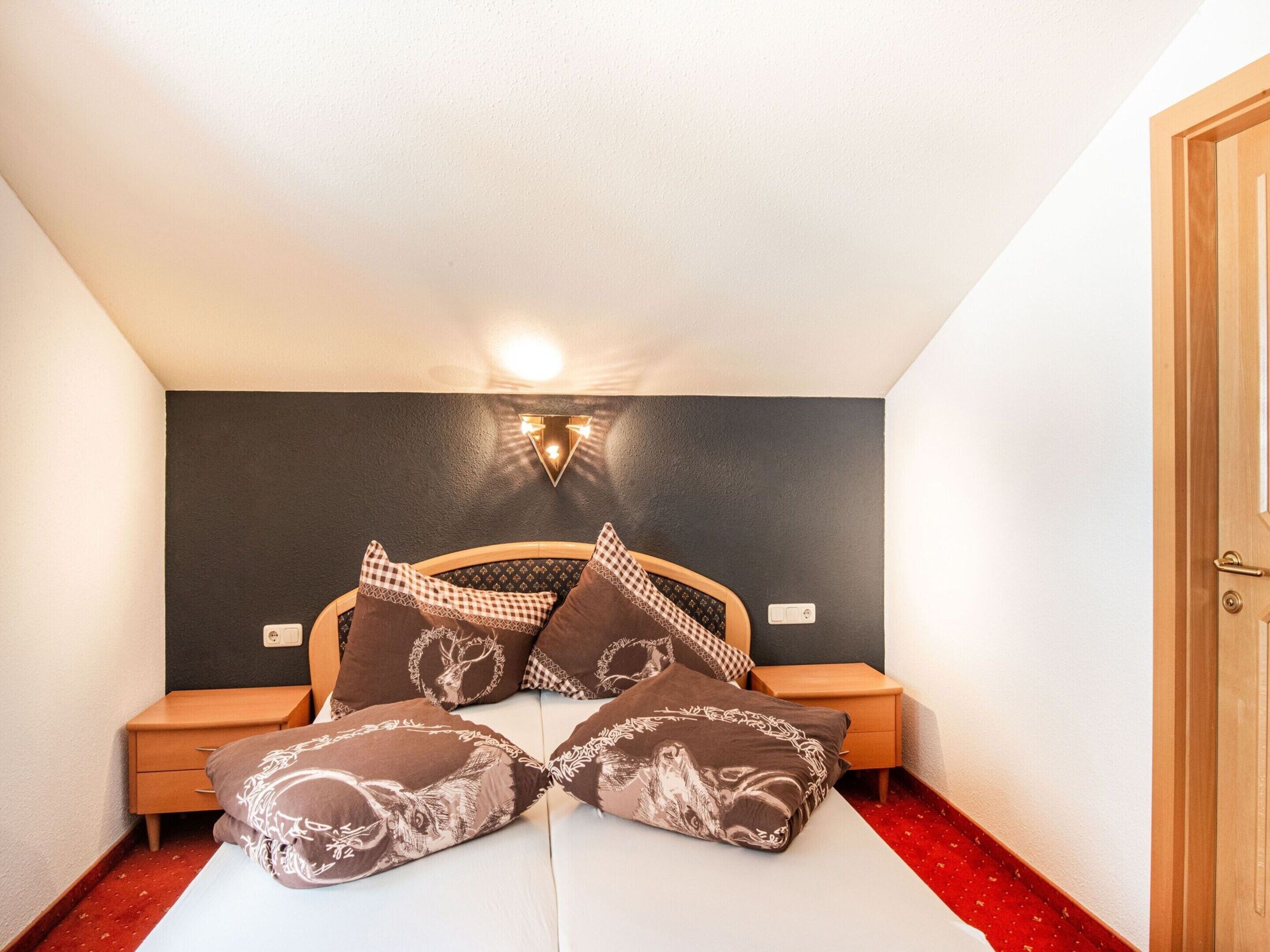 Ein kleines, gemütliches Schlafzimmer mit einem Bett, zwei Nachttischen, einer Wandleuchte und einer Tür.