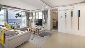 A modern living room with a sofa, TV, and a view of the sea. - Château Du Soleil Phala (UMPER Ban Chang)