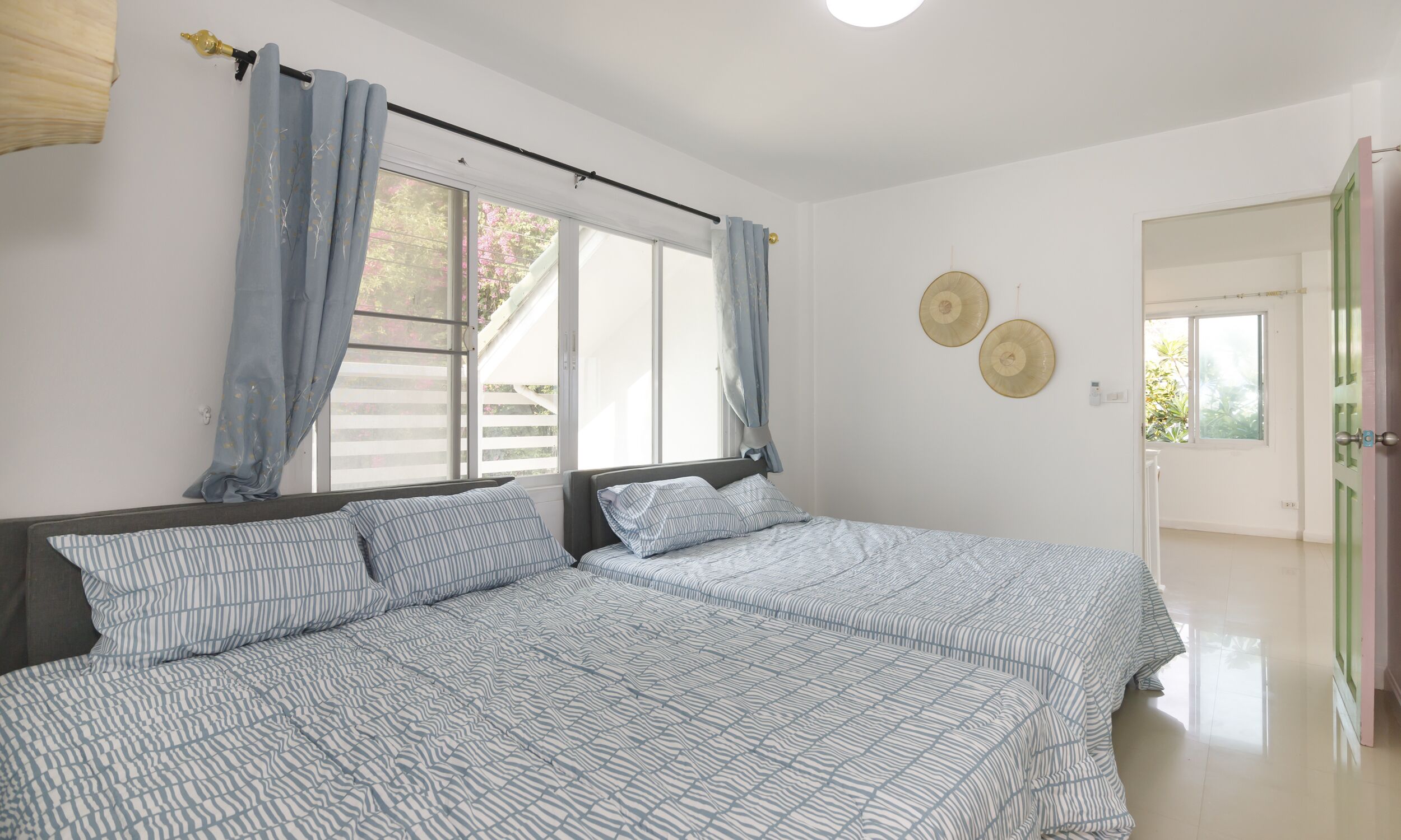 A bedroom with two beds, a window with curtains, and a door leading to another room.