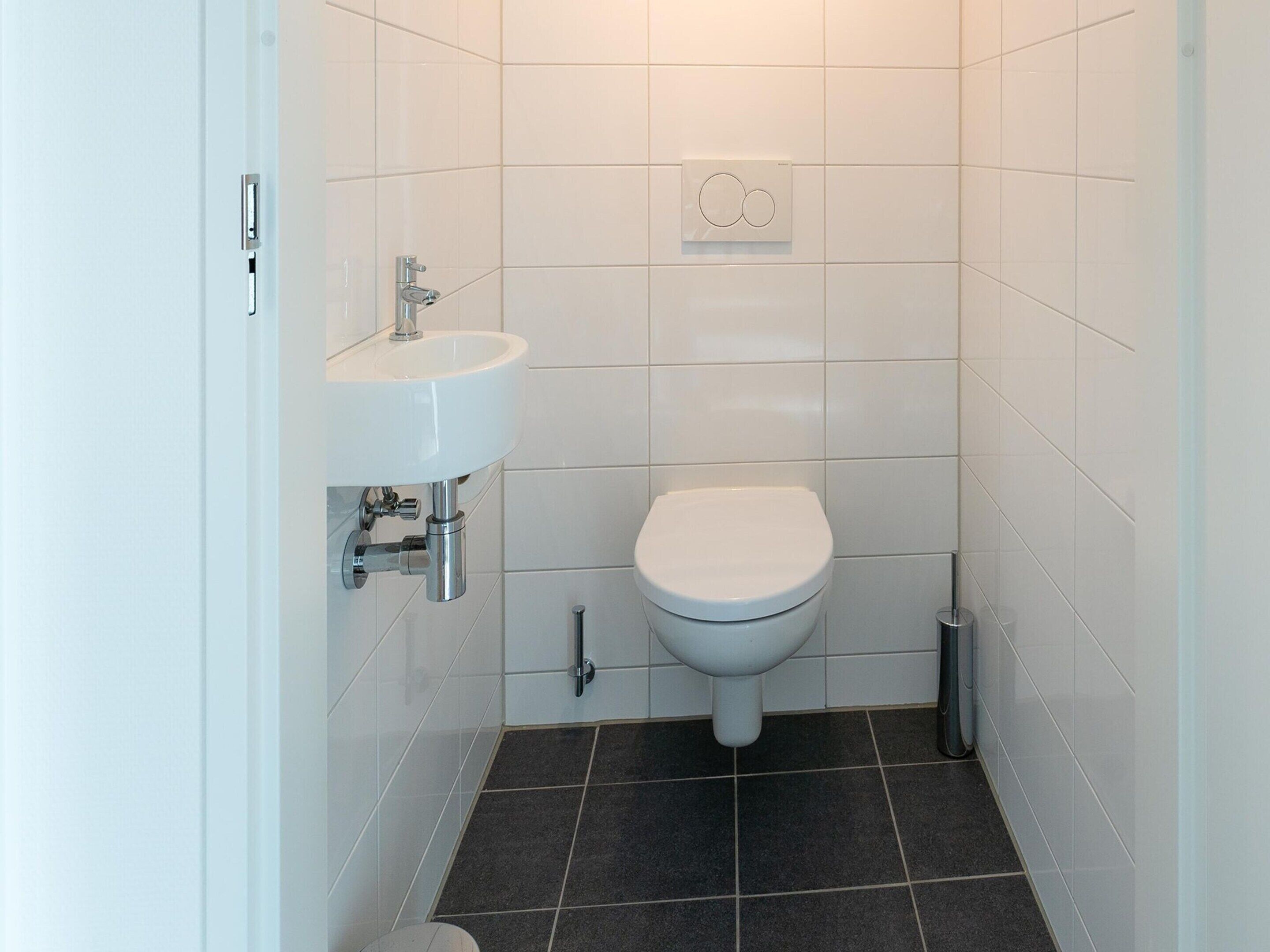A small, clean bathroom with a white sink, toilet, and a wall-mounted heater.
