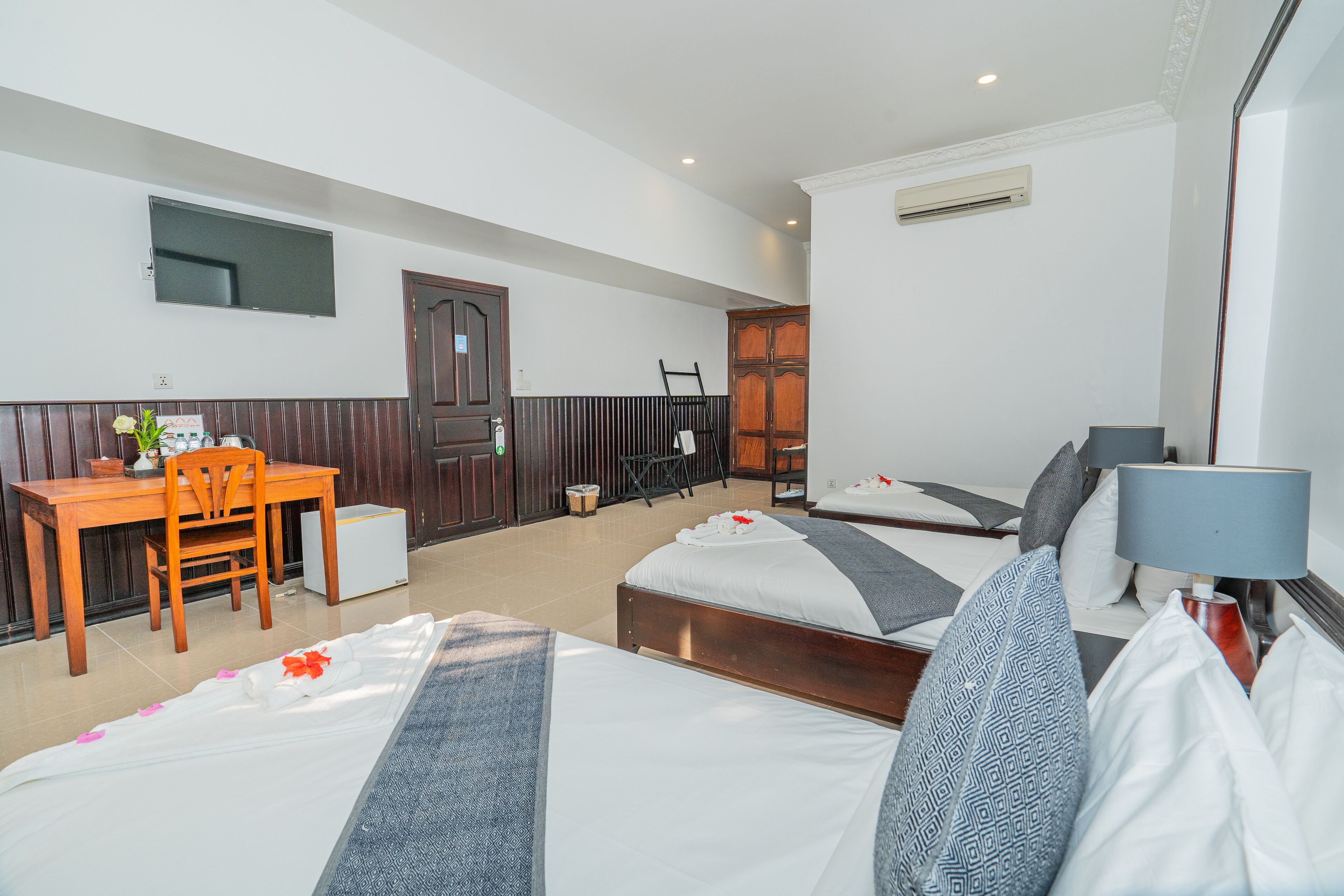 A hotel room with two beds, a desk, a chair, a TV, and an air conditioning unit.