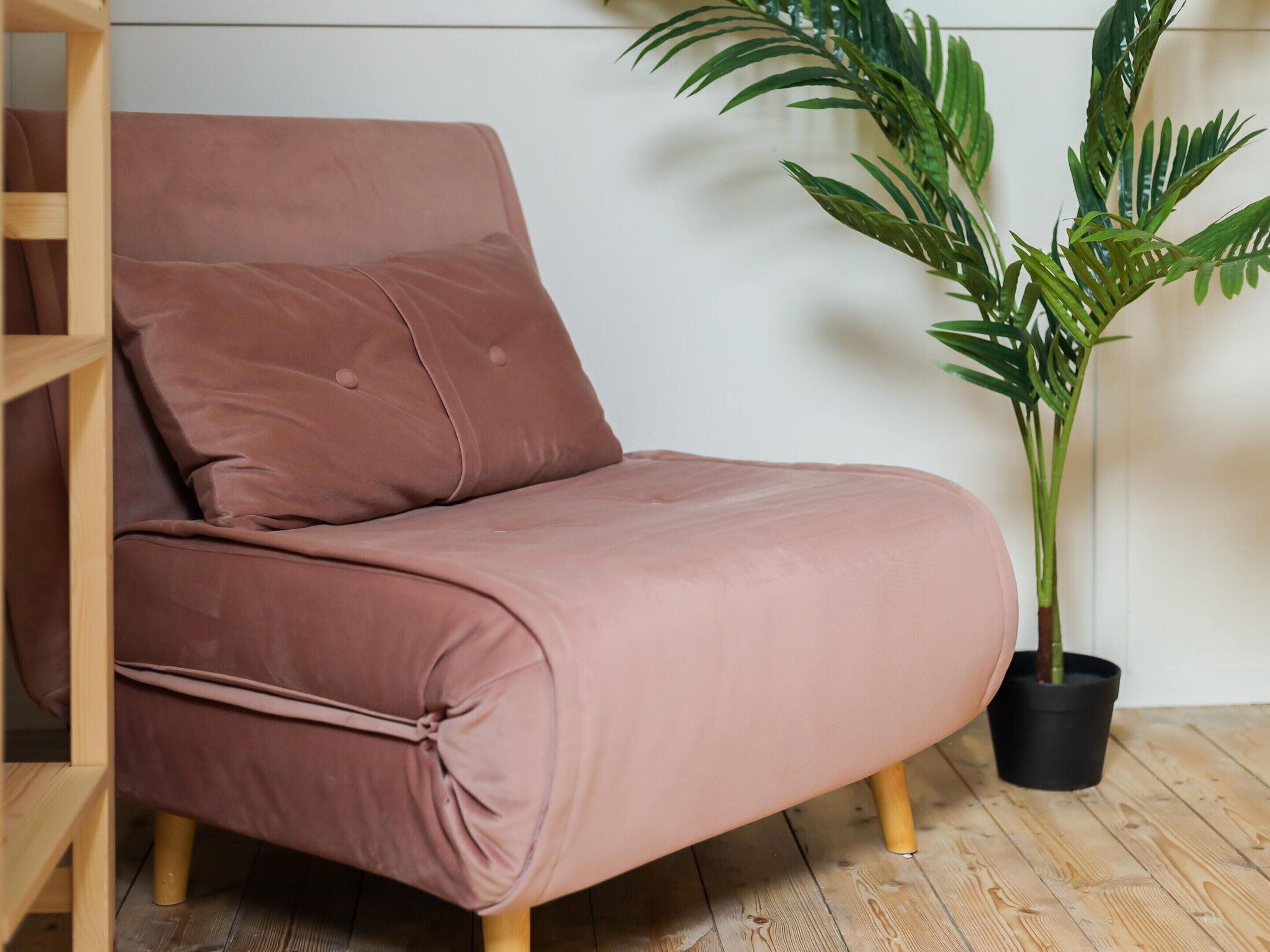 A brown sofa with wooden legs, positioned against a white wall, next to a potted plant.
