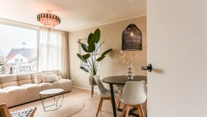 A modern living room with a sofa, a dining table with chairs, a large plant, and a hanging light fixture. - Suite in Vrouwenpolder Near North Sea Beach (Vrouwenpolder)