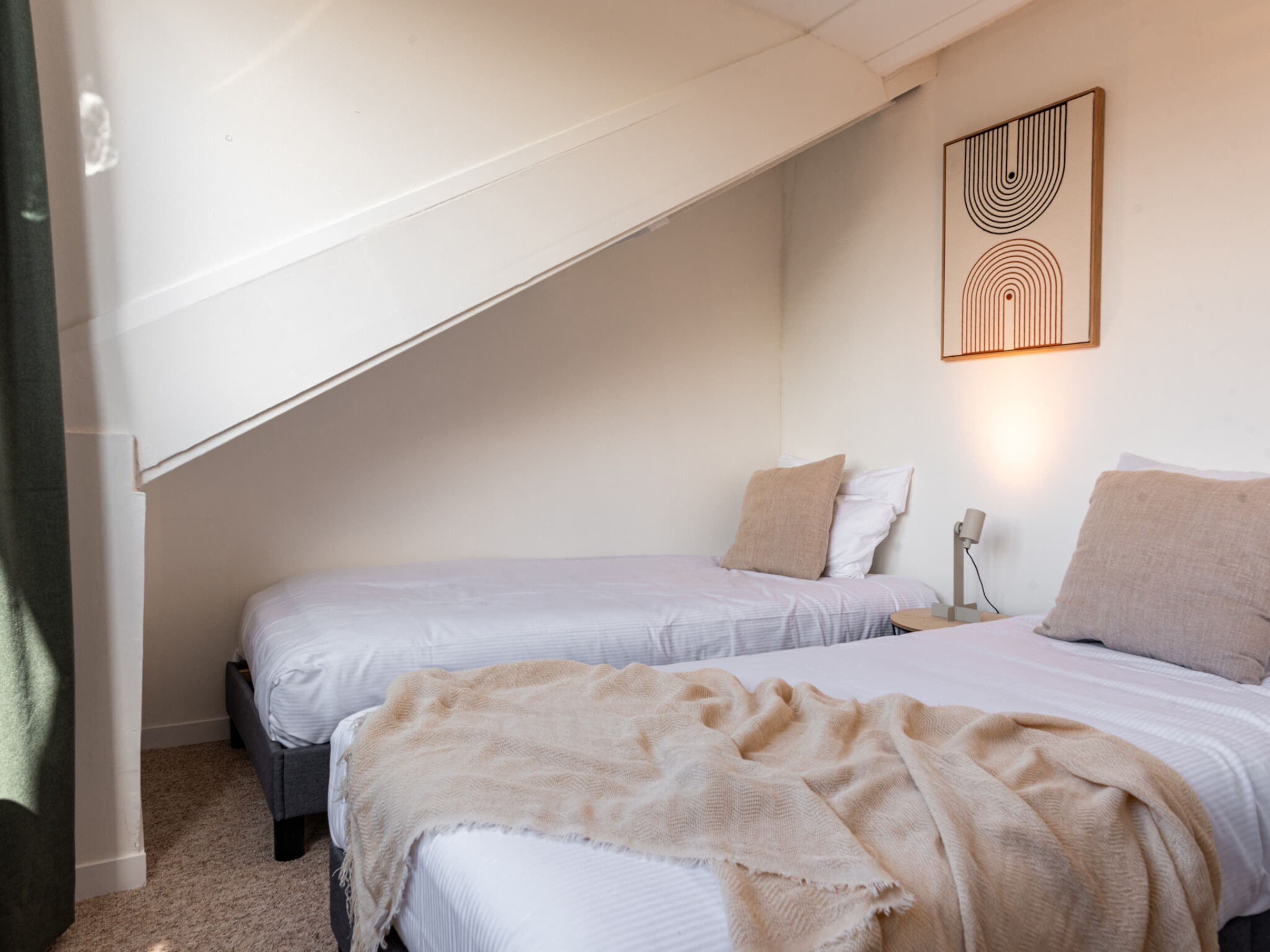 A bedroom with two beds, a sloped ceiling, and a wall-mounted artwork.