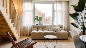 A modern living room with a wooden staircase, a sofa, a coffee table, and a large plant. - Suite in Vrouwenpolder Near North Sea Beach (Vrouwenpolder)