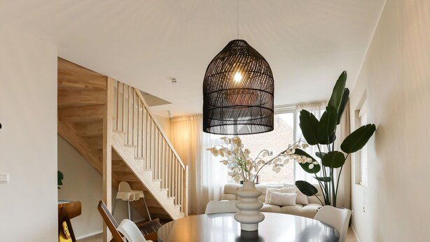 A dining area with a round table, white chairs, a black pendant light, and a staircase in the background. - Suite in Vrouwenpolder Near North Sea Beach (Vrouwenpolder)