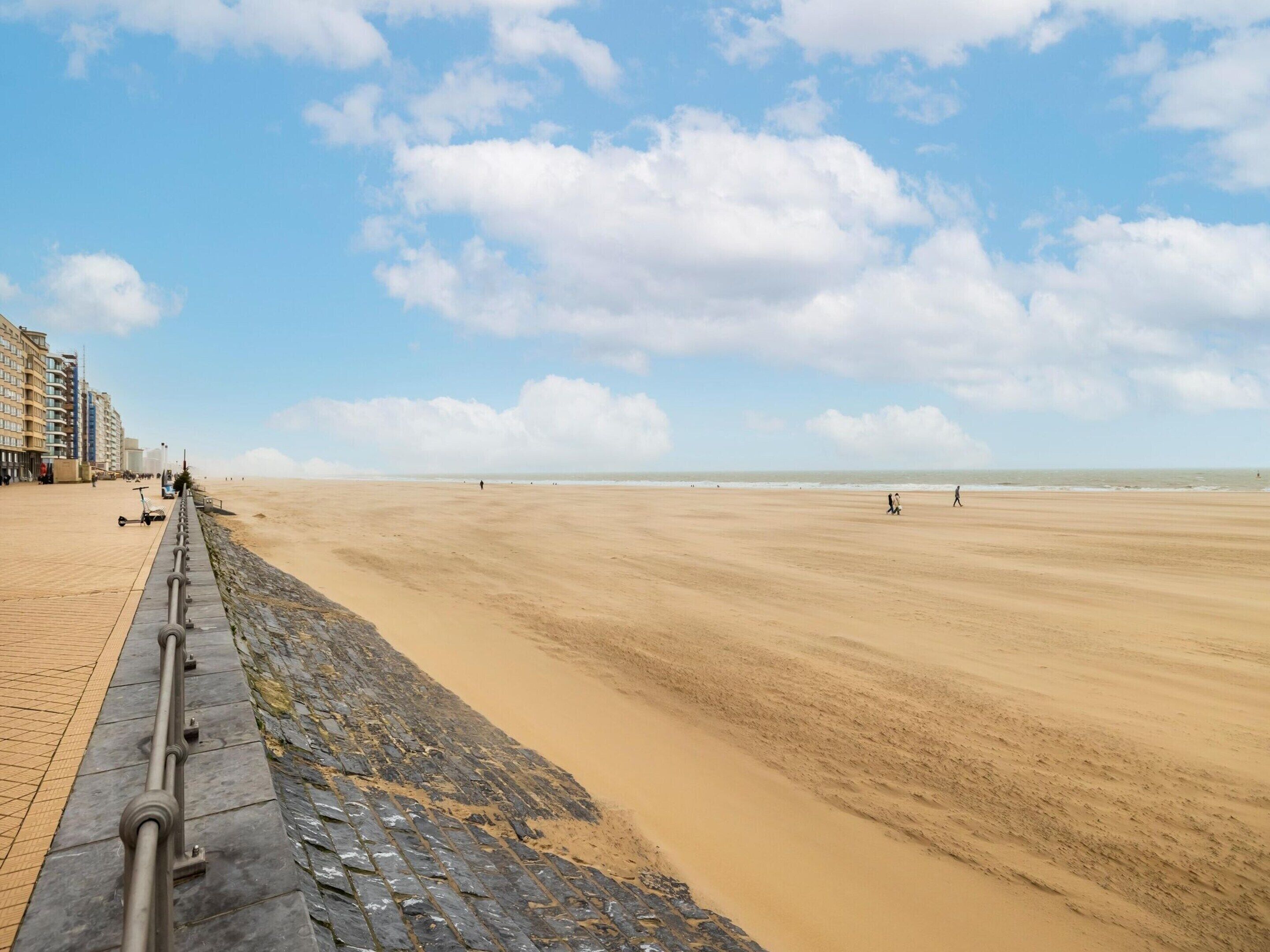 A sandy beach with a paved walkway and buildings in the background.