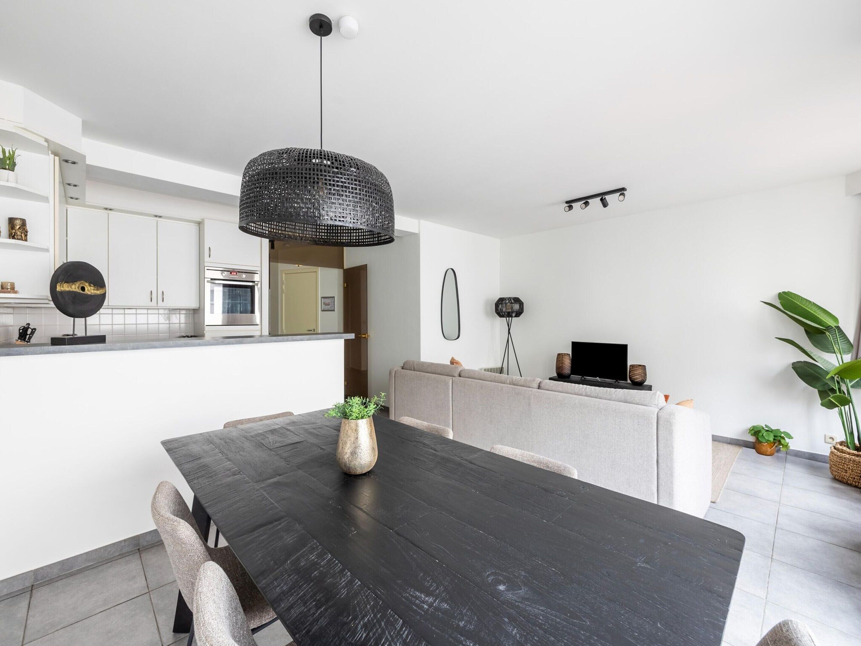 Una cocina moderna con armarios blancos, un comedor con mesa negra y una lámpara colgante.