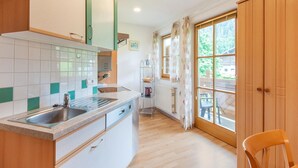 A modern kitchen with a large window, wooden cabinets, and a dining area with a chair. - Apartment With E-charging Station (Radstadt)