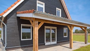 Une maison à deux étages dotée d’un patio couvert, de grandes fenêtres et d’un toit en pente.