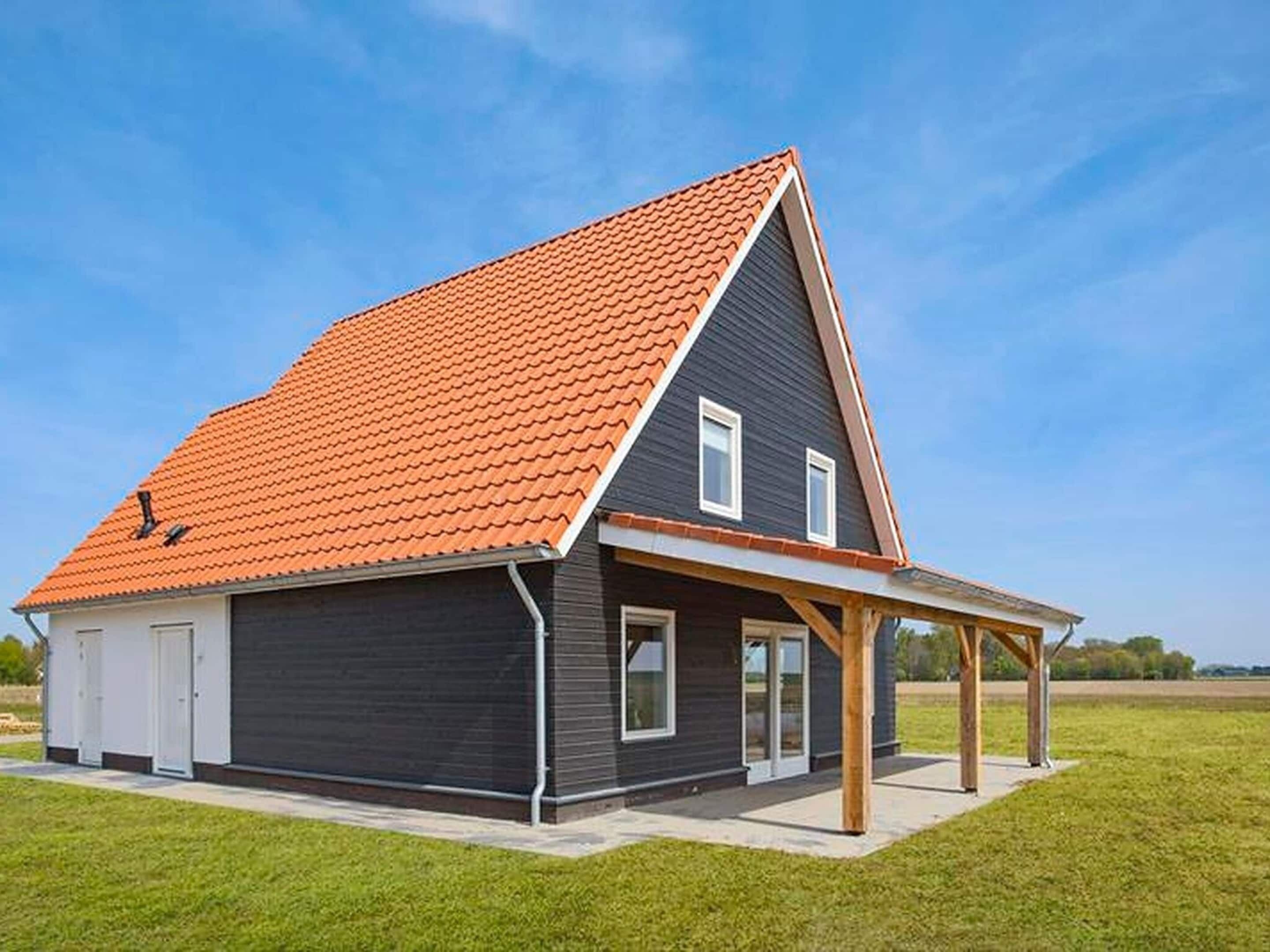 A modern two-story house with a dark exterior, a red-tiled roof, and a covered porch.