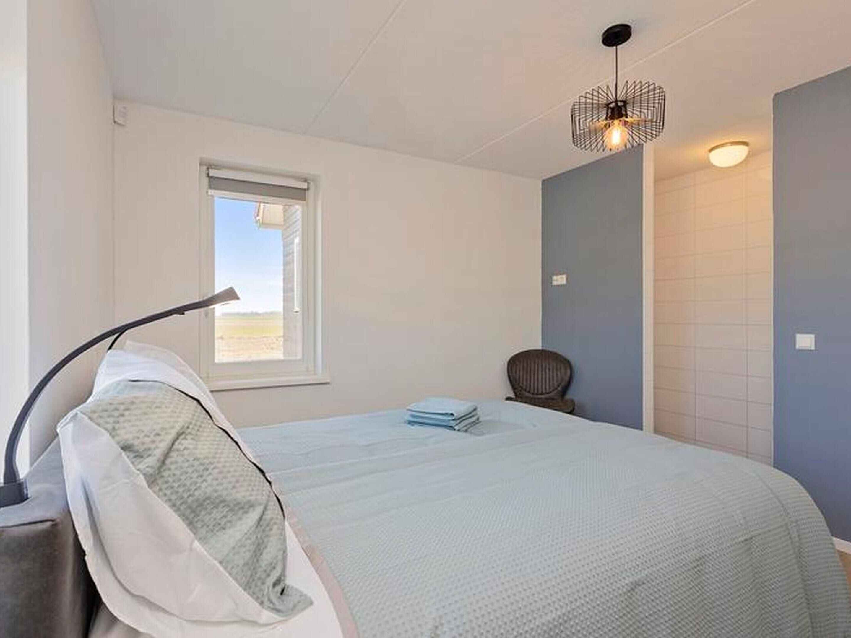 A bedroom with a bed, a chair, a desk, a lamp, a window, and a wall-mounted light fixture.