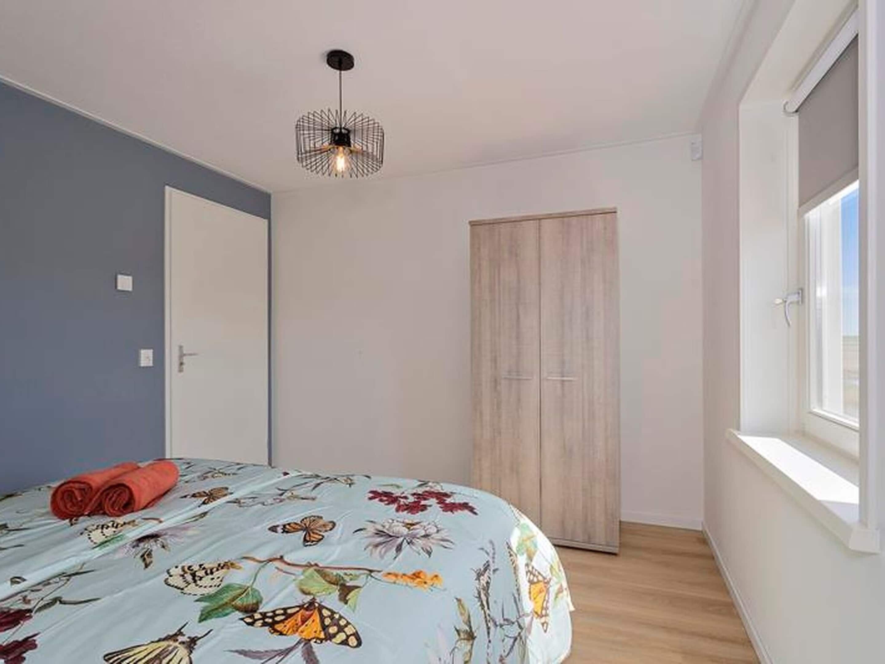 A bedroom with a bed, a wardrobe, a window, and a hanging light fixture.