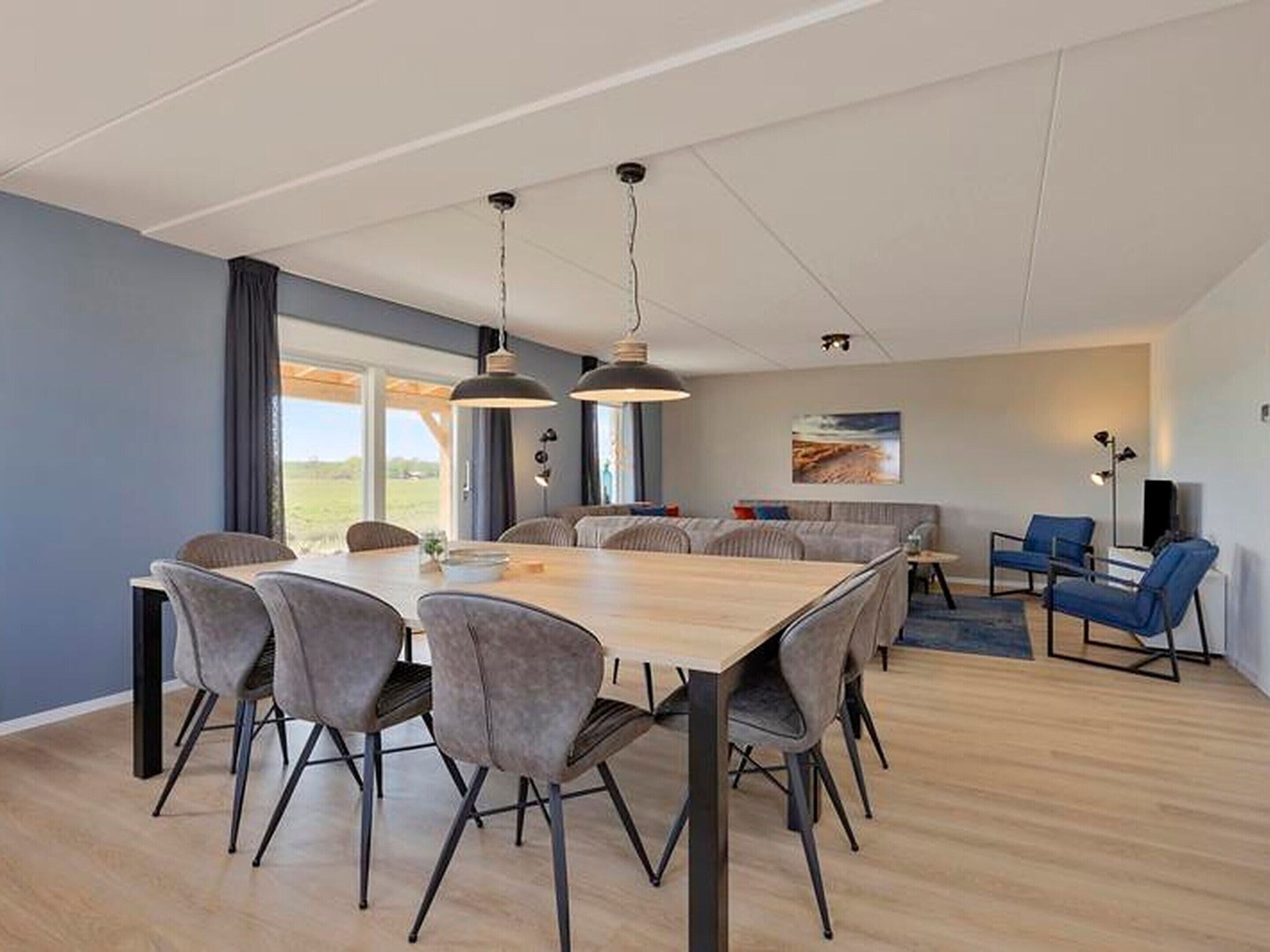 A modern dining area with a wooden table and grey upholstered chairs, a sofa, and a TV.