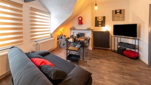 A cozy living room with a sofa, a dining area with a table and chairs, a fireplace, and a TV on a stand. - Nice Apartment in Liege With Parking (Liege)
