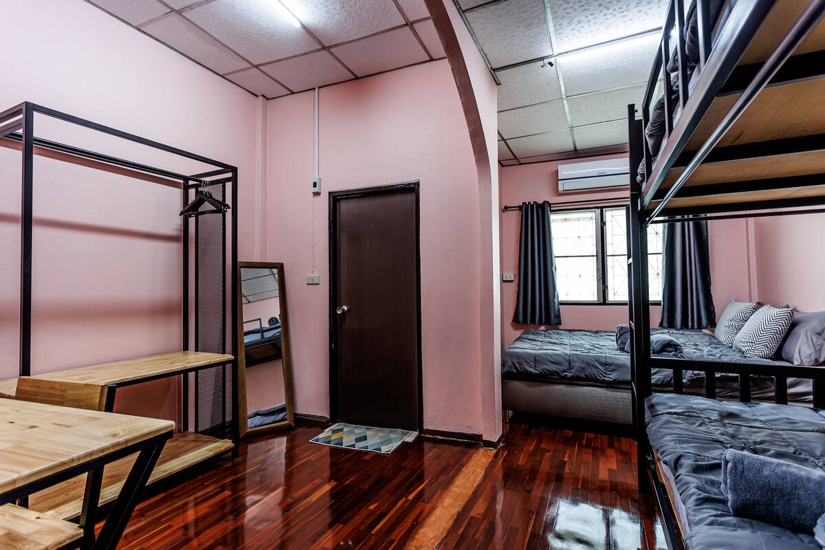 A dormitory room with bunk beds, a wooden desk, and a door.