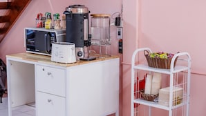 A kitchen with a microwave, toaster, coffee maker, and a basket of snacks on a white countertop. - Baan Mee Suk Ayutthaya (Ayutthaya)
