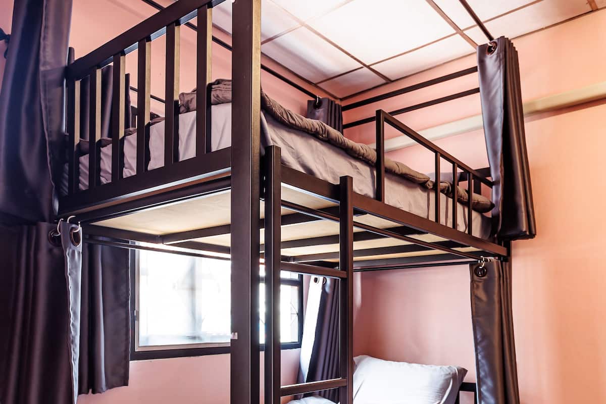 A bunk bed with a window, curtains, and a wooden floor.