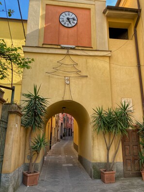 An arched passageway with a clock above, flanked by potted plants and a yellow building facade. - Italian old world charm with amazing view near Cinque Terre CITRA 011002-LT-0160 (Arcola)