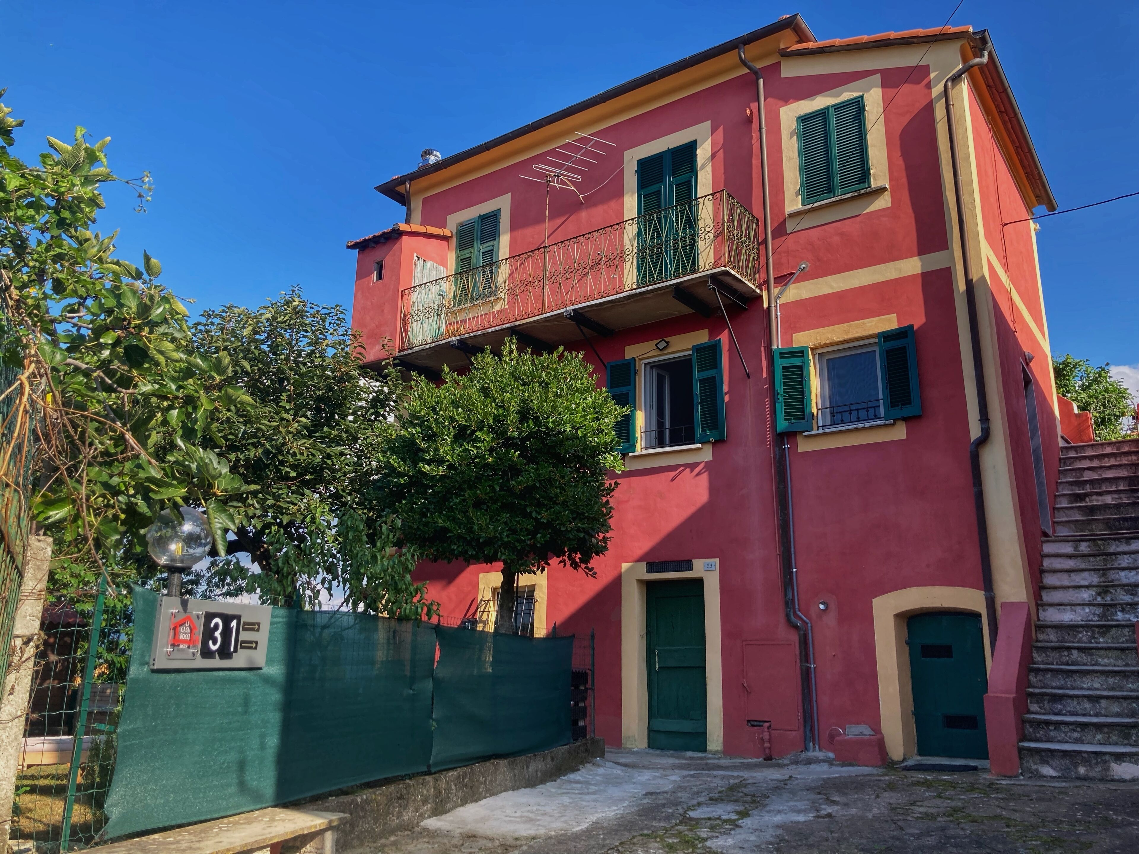 A red building with green shutters, a balcony, and a green fence.