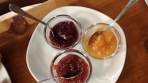 A white plate with two small glass bowls containing different colored jams, each with a spoon.